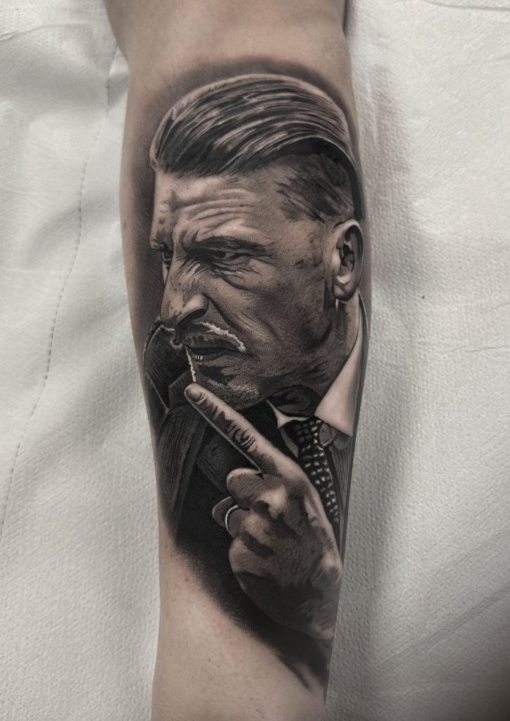 Retrato realista de un hombre con expresión seria tatuado en el antebrazo